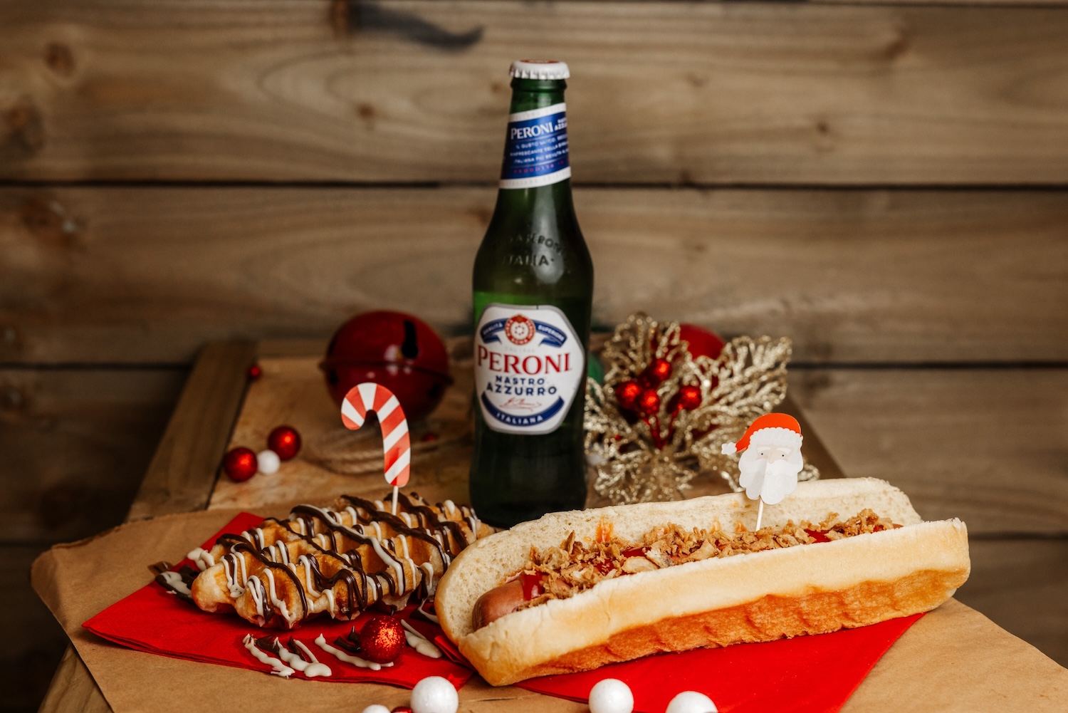 Peroni, bratwurst hot dog and chocolate waffle on a wooden table