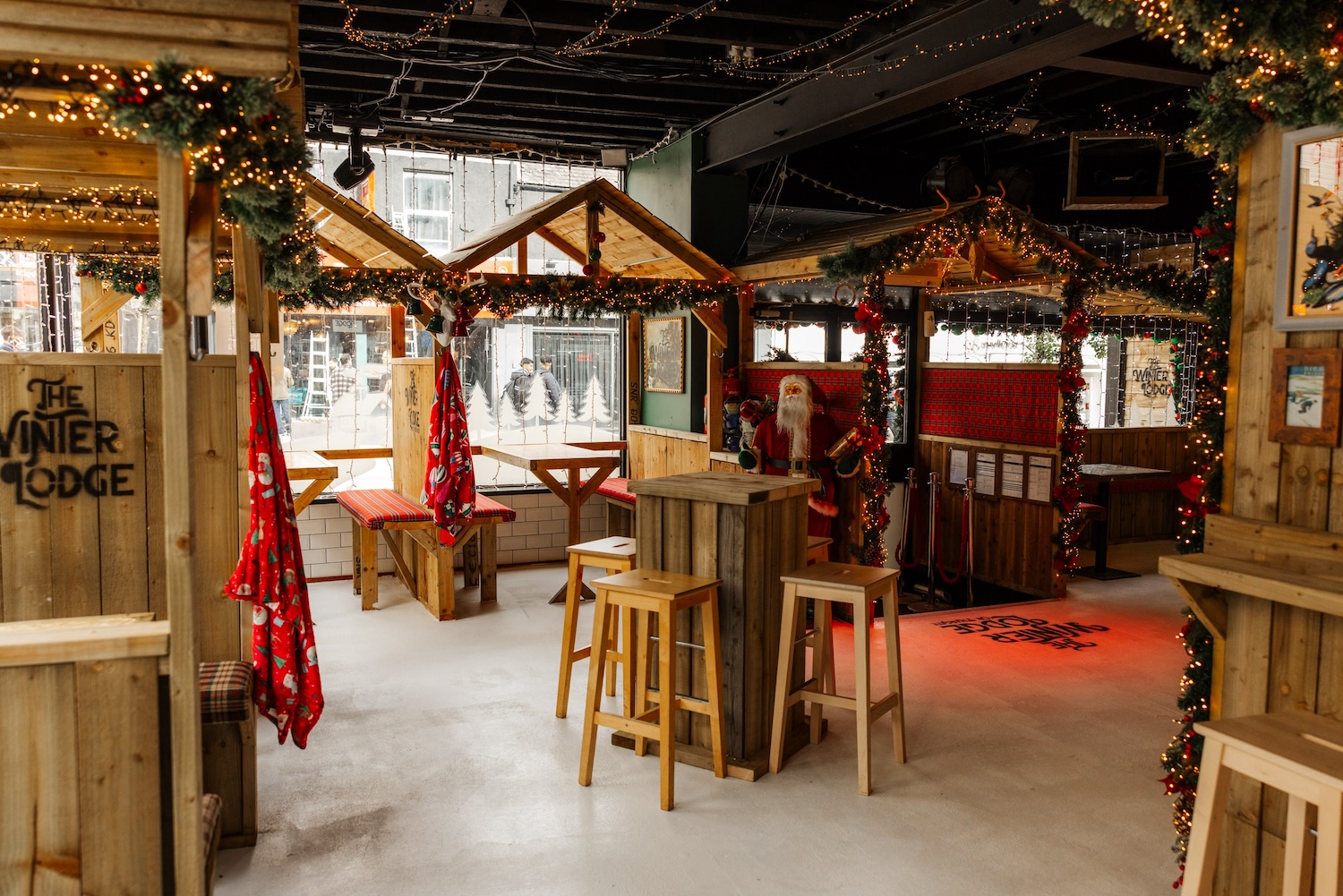 Inside The Winter Lodge — wooden huts, garlands and fairy lights, with Santa by the bar